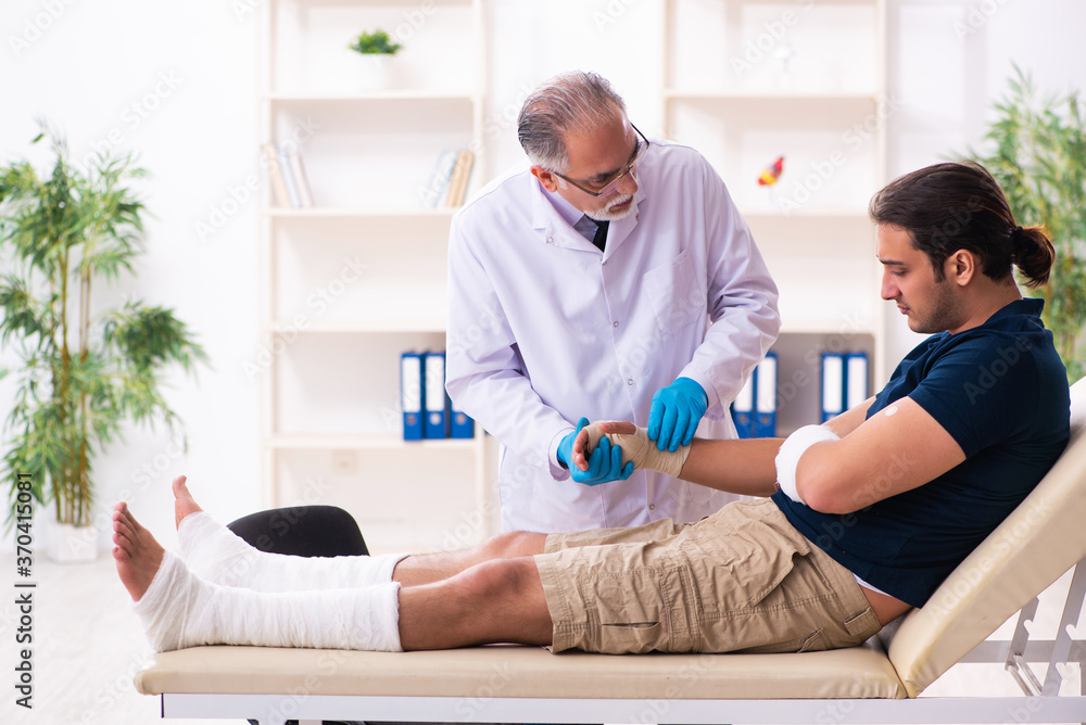 Fototapeta premium Young injured man visiting old doctor traumatologist