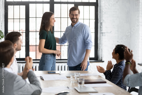Smiling executive introducing new hired team member to diverse employees at corporate meeting, workers applauding to successful employee, cheering, congratulating with job promotion at briefing