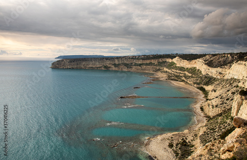 Coastal rocky seascape with cliffs and sea with cloudy stormy sky at sunset.