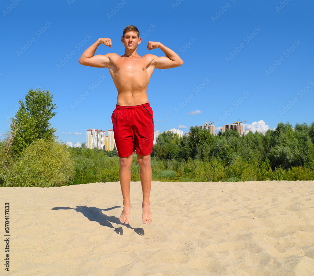 Young sporty naked guy in red shorts jumping on the sand