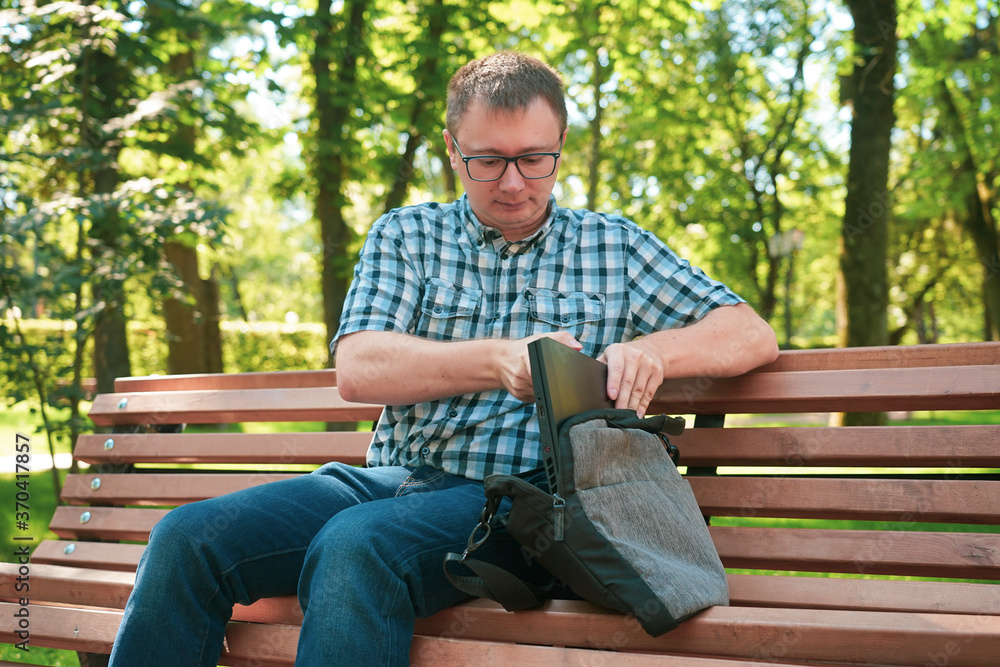 Fototapeta premium The guy sits in the park and works at a laptop.