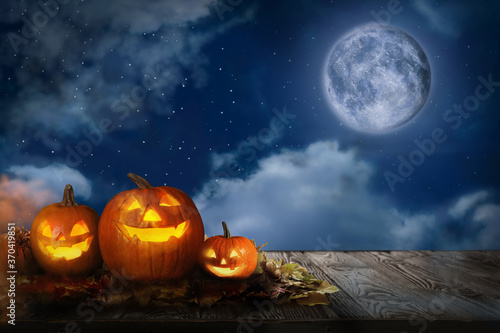 Scary Jack O Lantern pumpkins under full moon on Halloween. Space for text