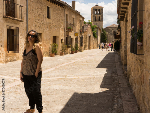 Blonde girl with sunglasses with a cobbled floor and stone houses in the background