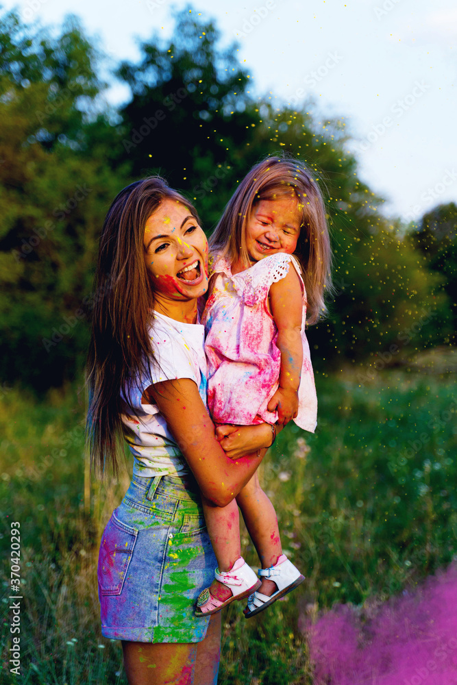 beautiful mom and daughter play with Hol colors. multi-colored paint on clothes and face.