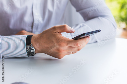 Image of hands of a man who is sitting at a table holding a phone
