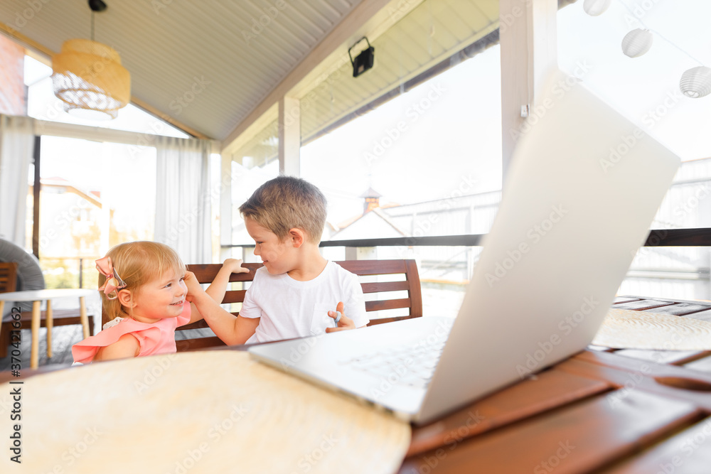 Obraz premium Small smiling kids brother and sister laugh and play laptop, communicate video conference chatting. Spacious cozy home interior.