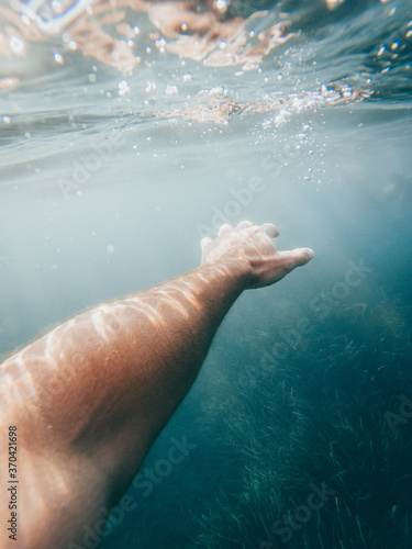 Vertical photo of white man's arm under crystal clear sea water with algae under it