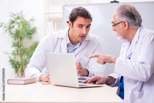 Experienced doctor teaching young male assistant using computer