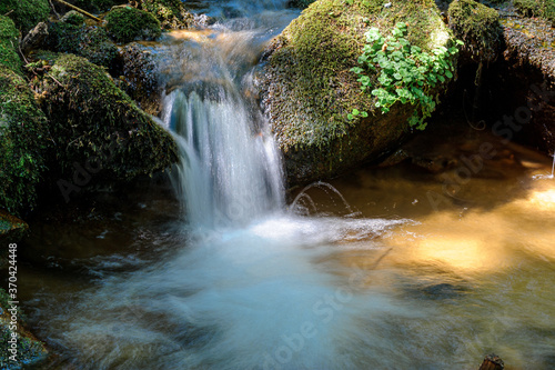 A small stream flows through the mossy rocks. Blurred water movement obtained with a slow shutter time.