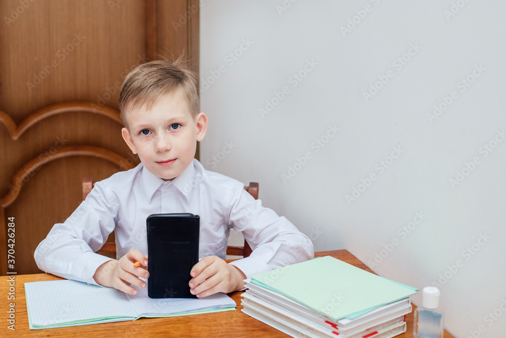 a boy of European appearance in a white shirt sits at a table and holds his head a boy of European appearance in a white shirt sits at a table and holds his head