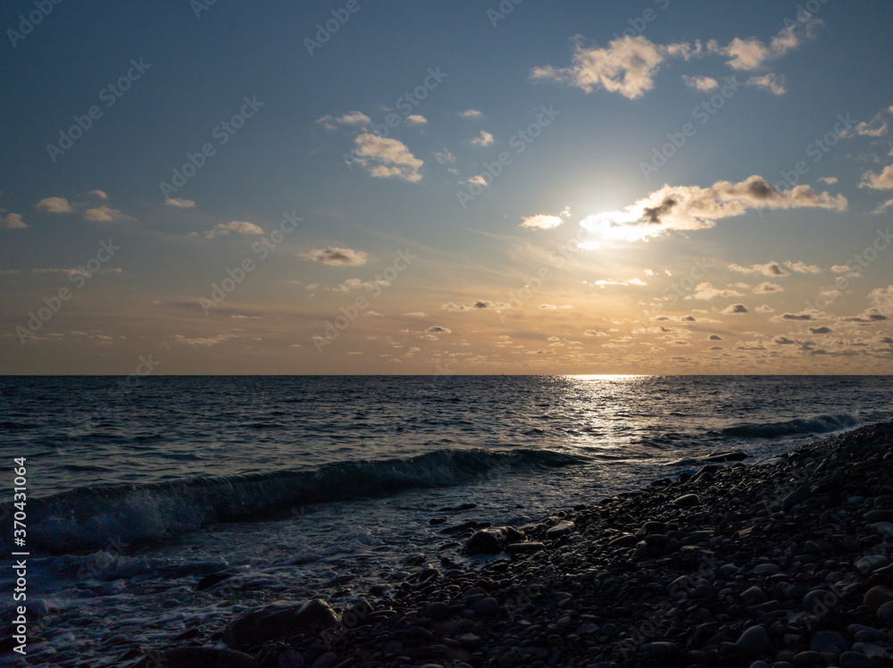 Obraz premium Sunset seascape, sunlight track along the water, sun in the clouds, wave runs on the pebble shore