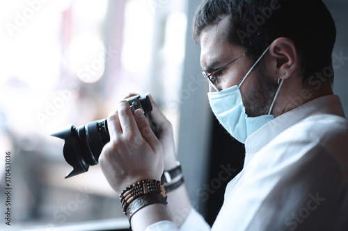 Turkish creative stylish man holding a camera and looking the images that he took with protective mask