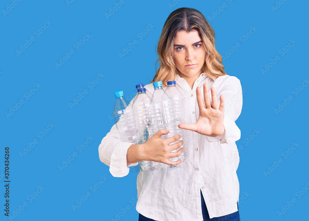 Young caucasian woman holding recycling plastic bottles with open hand doing stop sign with serious and confident expression, defense gesture Young caucasian woman holding recycling plastic bottles with open hand doing stop sign with serious and confident expression, defense gesture