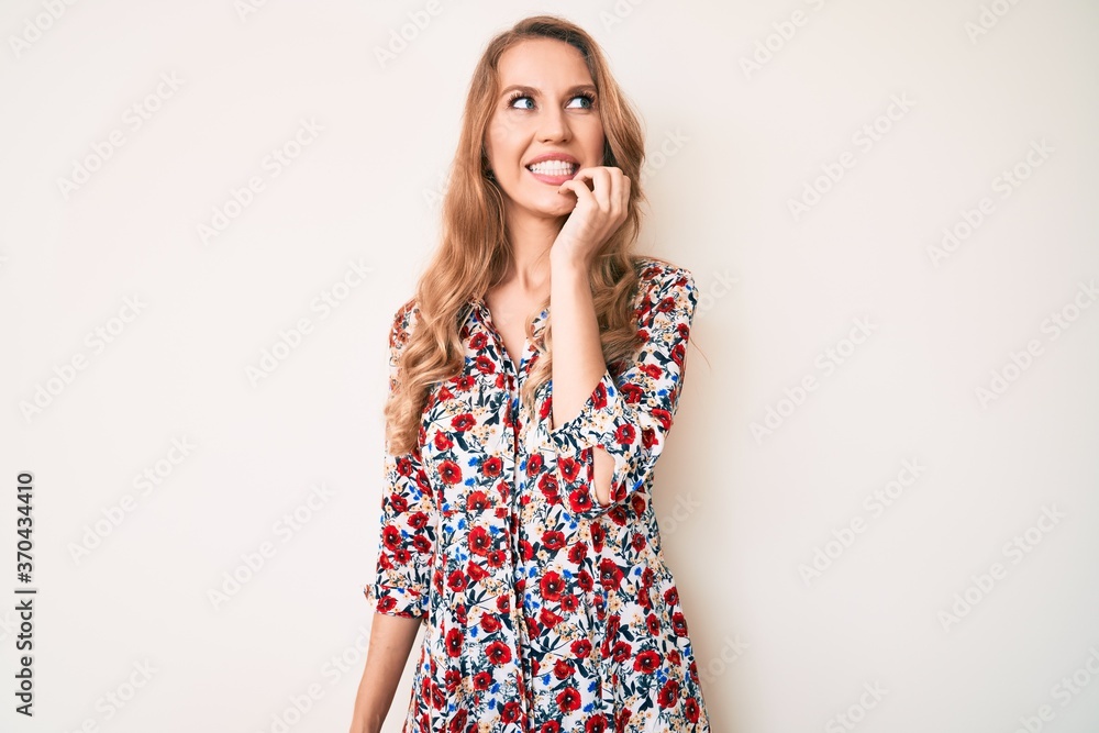 Young caucasian woman with blond hair wearing summer dress looking stressed and nervous with hands on mouth biting nails. anxiety problem. Young caucasian woman with blond hair wearing summer dress looking stressed and nervous with hands on mouth biting nails. anxiety problem.