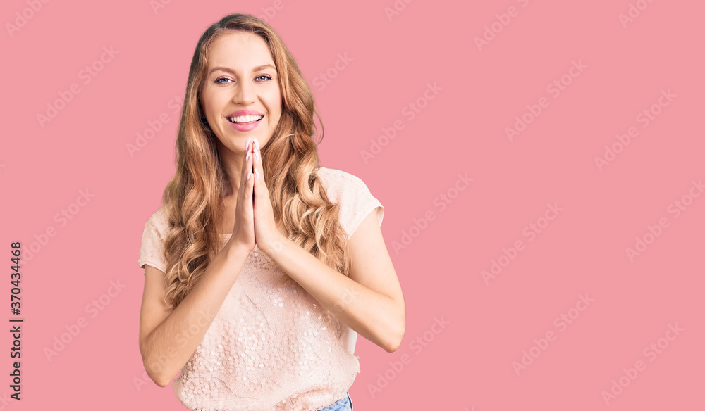Young beautiful caucasian woman with blond hair wearing casual clothes praying with hands together asking for forgiveness smiling confident. Young beautiful caucasian woman with blond hair wearing casual clothes praying with hands together asking for forgiveness smiling confident.