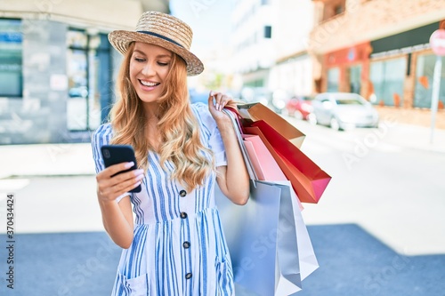 Young beautiful shopper woman smiling happy going to the shops sales holding shopping bags ourtdoors, smiling happy using smartphone photo