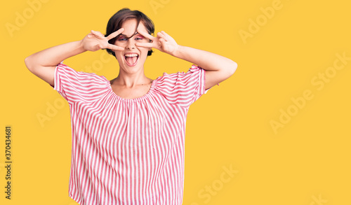 Beautiful young woman with short hair wearing casual summer clothes doing peace symbol with fingers over face, smiling cheerful showing victory © Krakenimages.com