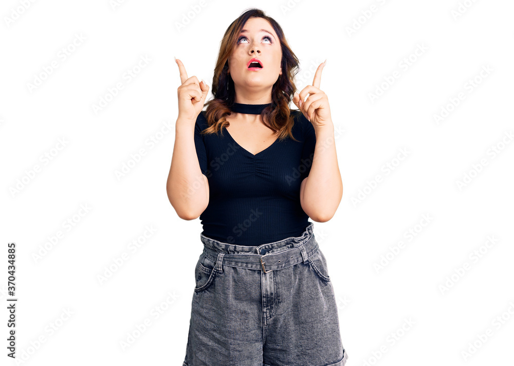Young beautiful caucasian woman wearing casual clothes amazed and surprised looking up and pointing with fingers and raised arms. Young beautiful caucasian woman wearing casual clothes amazed and surprised looking up and pointing with fingers and raised arms.