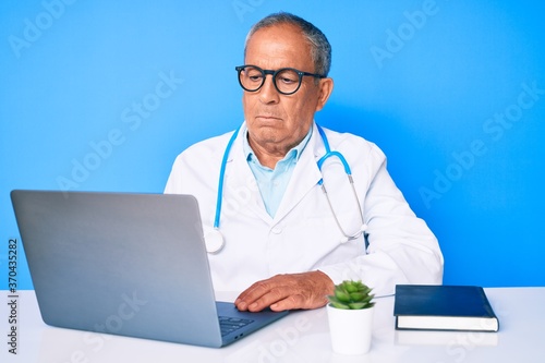 Senior handsome man with gray hair wearing doctor uniform working using computer laptop depressed and worry for distress, crying angry and afraid. sad expression. © Krakenimages.com