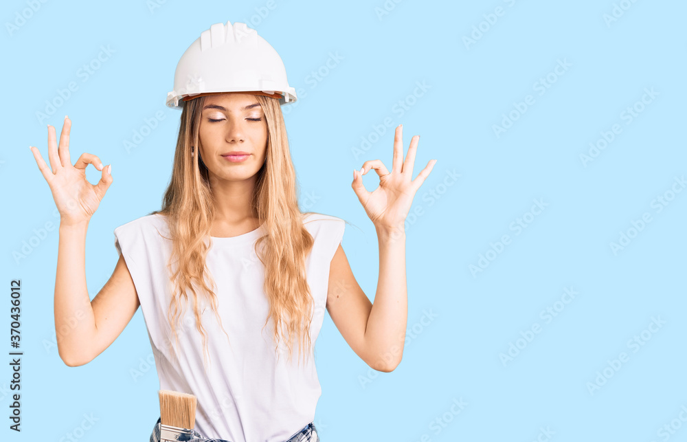 Beautiful caucasian woman with blonde hair wearing hardhat and painter clothes relax and smiling with eyes closed doing meditation gesture with fingers. yoga concept.