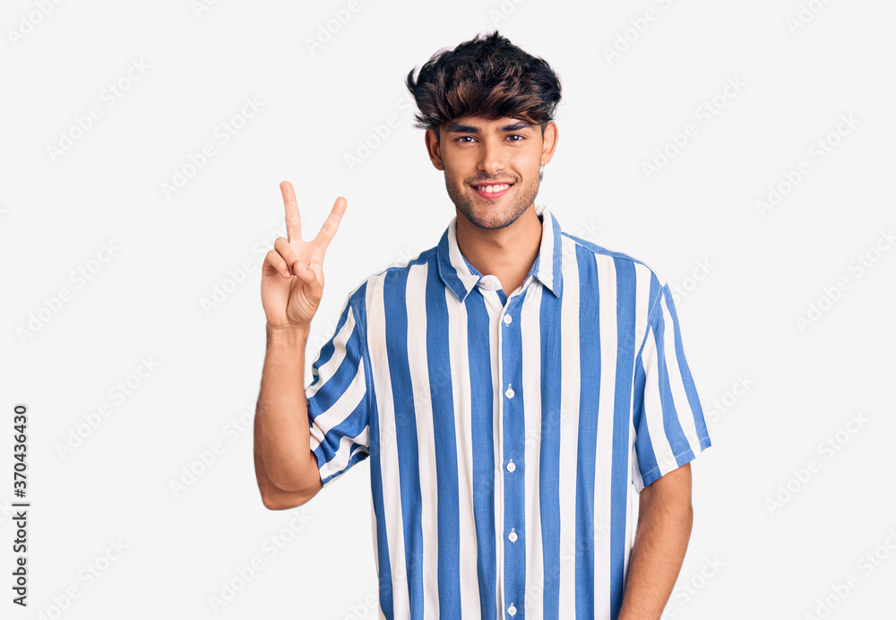 Young hispanic man wearing casual clothes smiling looking to the camera showing fingers doing victory sign. number two. Young hispanic man wearing casual clothes smiling looking to the camera showing fingers doing victory sign. number two.
