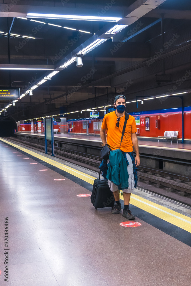 Tourist travel by metro in the coronavirus pandemic, safe travel, social distance, a new normal. A young man with a suitcase waiting for the subway