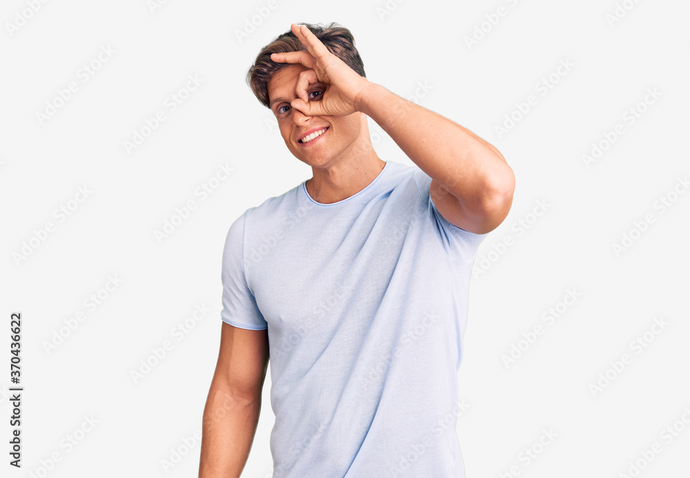 Young handsome man wearing casual clothes smiling happy doing ok sign with hand on eye looking through fingers Young handsome man wearing casual clothes smiling happy doing ok sign with hand on eye looking through fingers