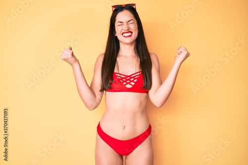 Young beautiful caucasian woman wearing bikini very happy and excited doing winner gesture with arms raised, smiling and screaming for success. celebration concept.