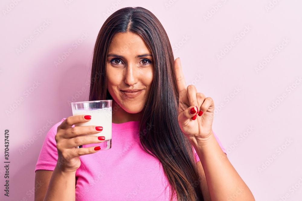 Young beautiful brunette woman drinking glass of milk smiling with an idea or question pointing finger with happy face, number one Young beautiful brunette woman drinking glass of milk smiling with an idea or question pointing finger with happy face, number one