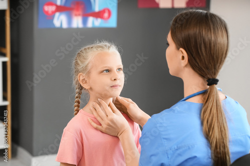 Doctor examining little girl with thyroid gland problem in clinic photo