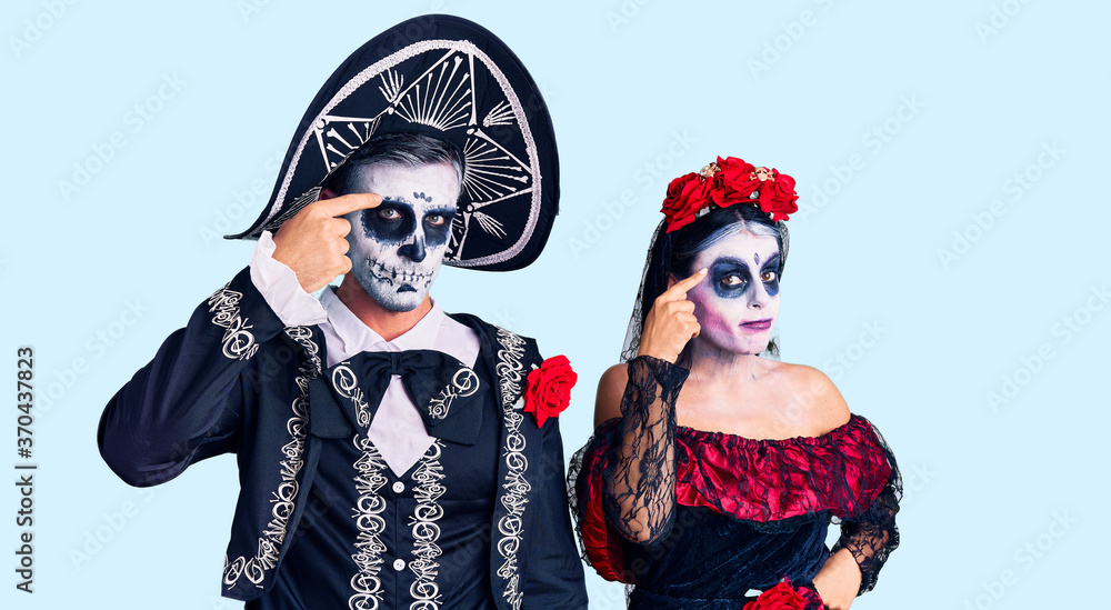 Young couple wearing mexican day of the dead costume over background pointing unhappy to pimple on forehead, ugly infection of blackhead. acne and skin problem