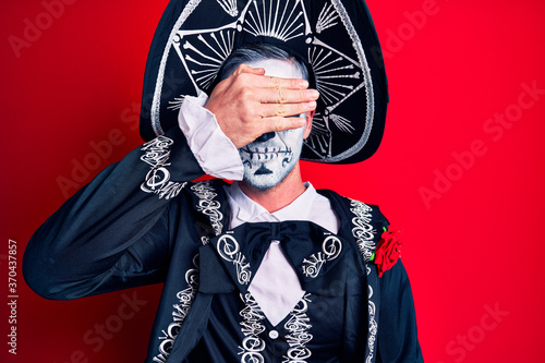 Young man wearing mexican day of the dead costume over red smiling and laughing with hand on face covering eyes for surprise. blind concept.