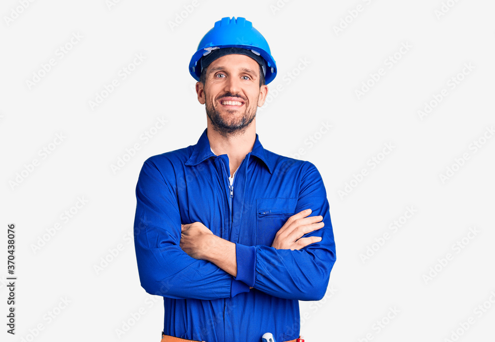 Young handsome man wearing worker uniform and hardhat happy face smiling with crossed arms looking at the camera. positive person. Young handsome man wearing worker uniform and hardhat happy face smiling with crossed arms looking at the camera. positive person.