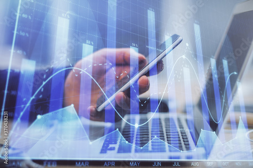 Double exposure of man's hands holding and using a phone and financial graph drawing. Analysis concept.