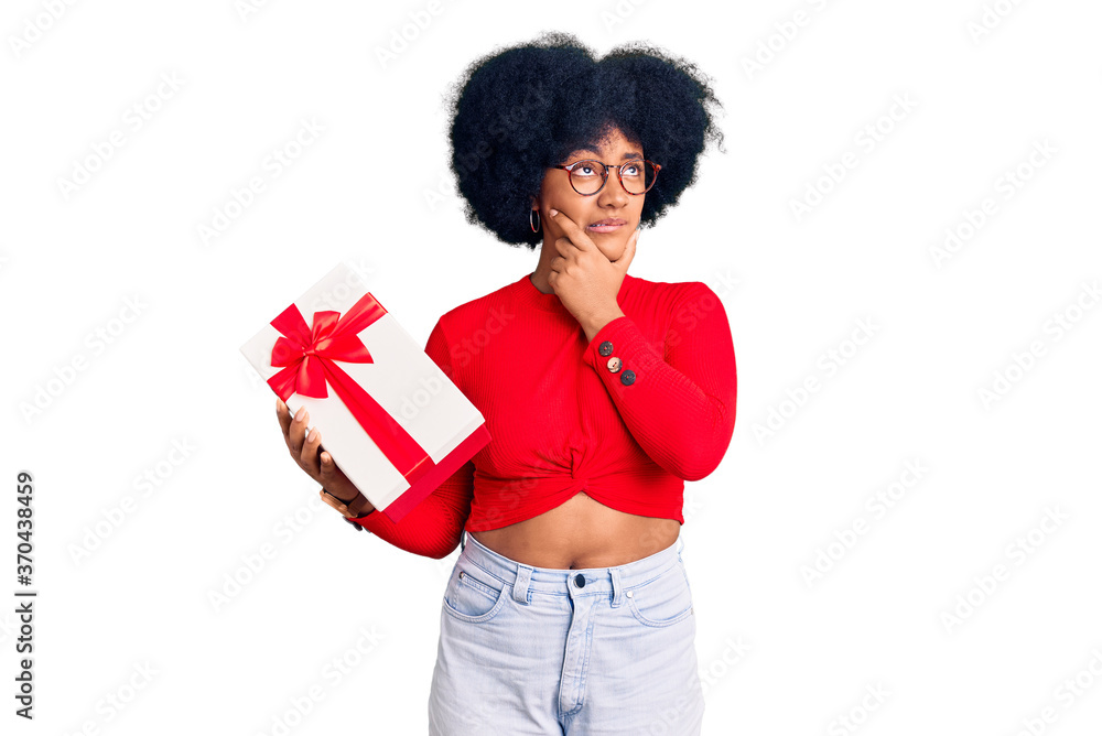 Young african american girl holding gift thinking worried about a question, concerned and nervous with hand on chin Young african american girl holding gift thinking worried about a question, concerned and nervous with hand on chin