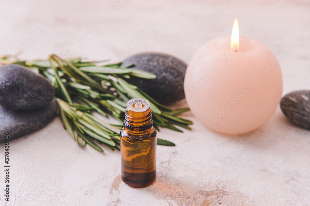 Bottle of rosemary essential oil, aroma candle and spa stones on light background