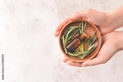 Female hands with bottle of rosemary oil on light background