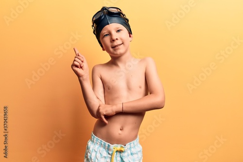 Cute blond kid wearing swimwear and swimmer glasses smiling happy pointing with hand and finger to the side © Krakenimages.com
