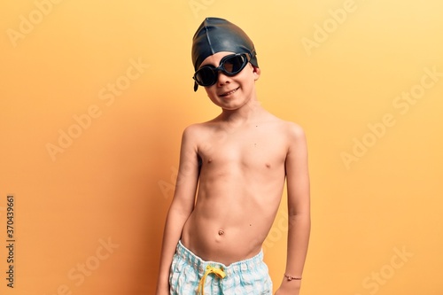 Cute blond kid wearing swimwear and swimmer glasses with a happy and cool smile on face. lucky person. © Krakenimages.com