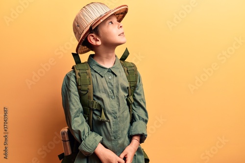 Cute blond kid wearing explorer hat and backpack looking to side, relax profile pose with natural face and confident smile. photo