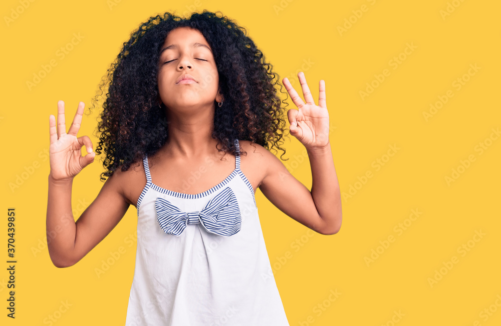 African american child with curly hair wearing casual clothes relax and smiling with eyes closed doing meditation gesture with fingers. yoga concept. African american child with curly hair wearing casual clothes relax and smiling with eyes closed doing meditation gesture with fingers. yoga concept.