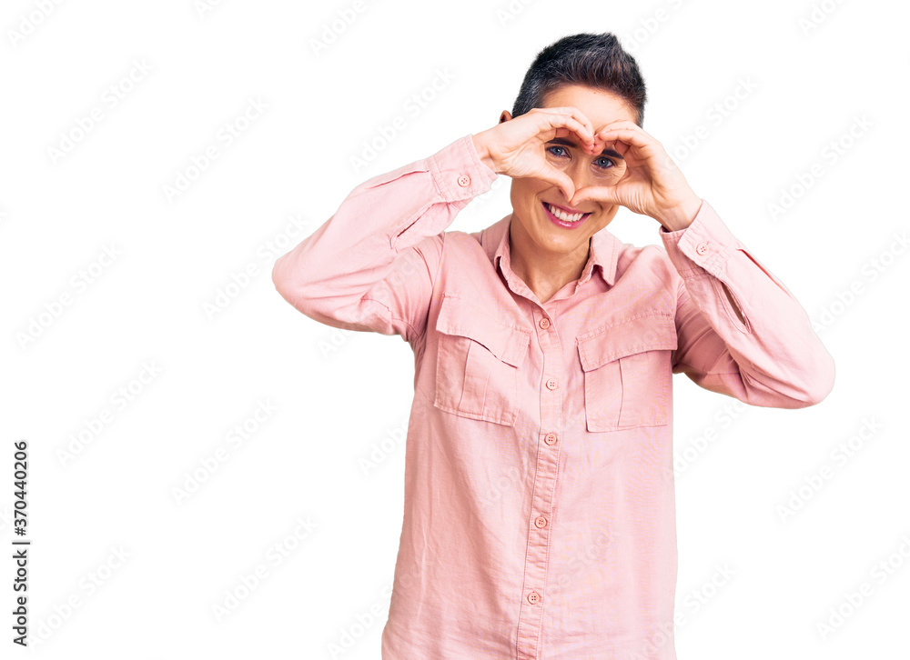 Young woman with short hair wearing casual clothes doing heart shape with hand and fingers smiling looking through sign Young woman with short hair wearing casual clothes doing heart shape with hand and fingers smiling looking through sign