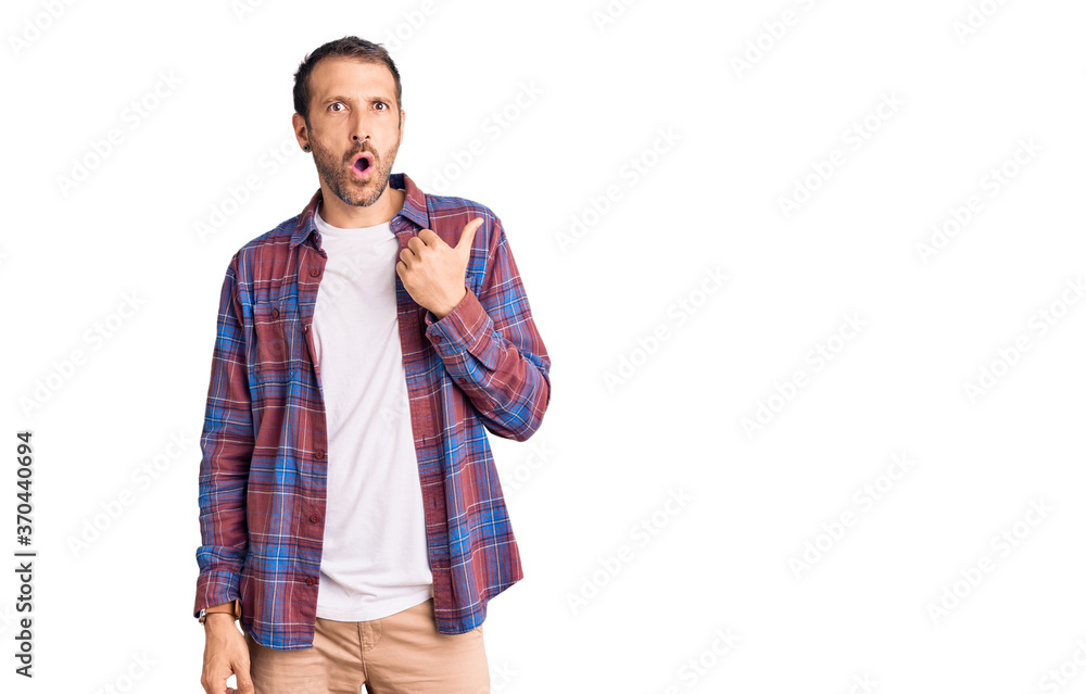 Young handsome man wearing casual clothes surprised pointing with hand finger to the side, open mouth amazed expression. Young handsome man wearing casual clothes surprised pointing with hand finger to the side, open mouth amazed expression.