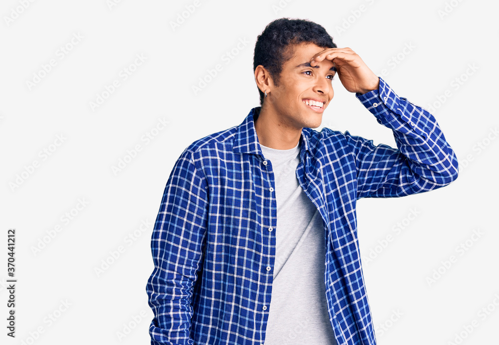 Young african amercian man wearing casual clothes very happy and smiling looking far away with hand over head. searching concept. Young african amercian man wearing casual clothes very happy and smiling looking far away with hand over head. searching concept.