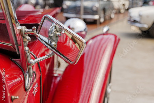 Selected focus detail of rectangular outdoor side mirror of red vintage and classic car.