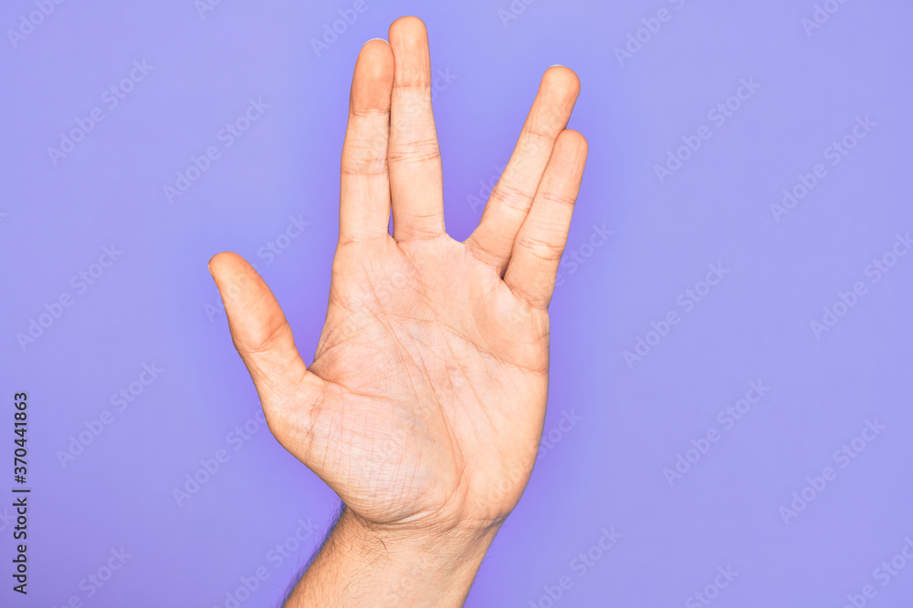 Hand of caucasian young man showing fingers over isolated purple background greeting doing Vulcan salute, showing hand palm and fingers, freak culture Hand of caucasian young man showing fingers over isolated purple background greeting doing Vulcan salute, showing hand palm and fingers, freak culture