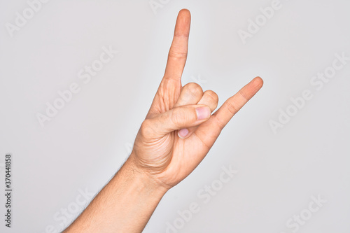 Hand of caucasian young man showing fingers over isolated white background gesturing rock and roll symbol, showing obscene horns gesture © Krakenimages.com