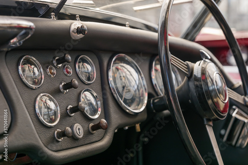Selective focus, interior view of classic and vintage detail of gauge, switches, button, meter and steering wheel on black leather control panel dashboard inside old antique convertible car. © Peeradontax