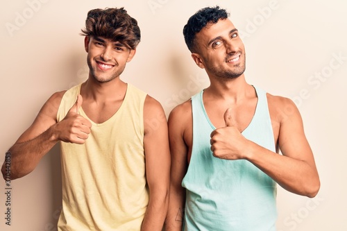 Young gay couple wearing casual clothes doing happy thumbs up gesture with hand. approving expression looking at the camera showing success. © Krakenimages.com