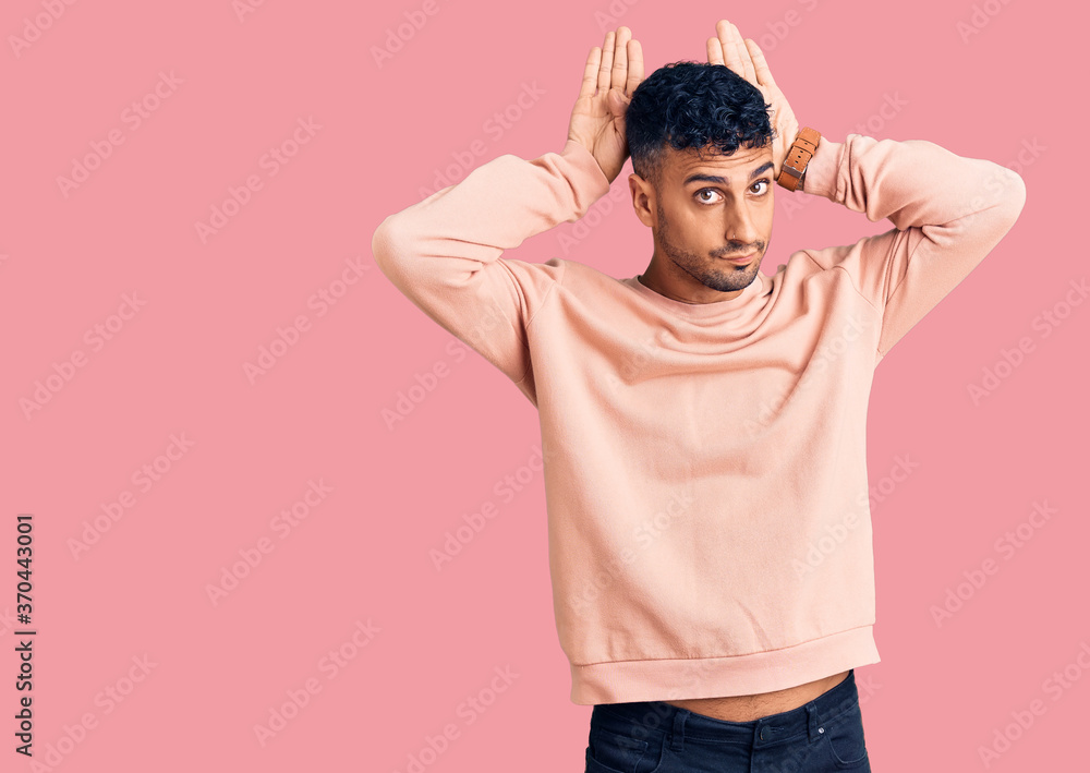Young hispanic man wearing casual clothes doing bunny ears gesture with hands palms looking cynical and skeptical. easter rabbit concept. Young hispanic man wearing casual clothes doing bunny ears gesture with hands palms looking cynical and skeptical. easter rabbit concept.